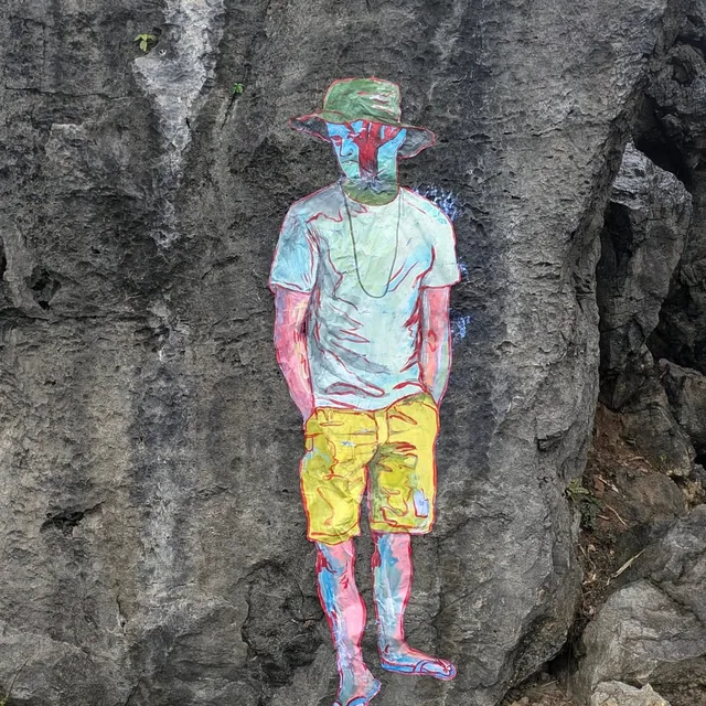 Collage sur une paroi rocheuse, personnage debout en tee-shirt et chapeau.
