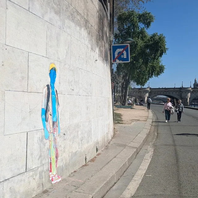 Collage sur un muret le long d'un quai, silhouette bleue étirée en hauteur.