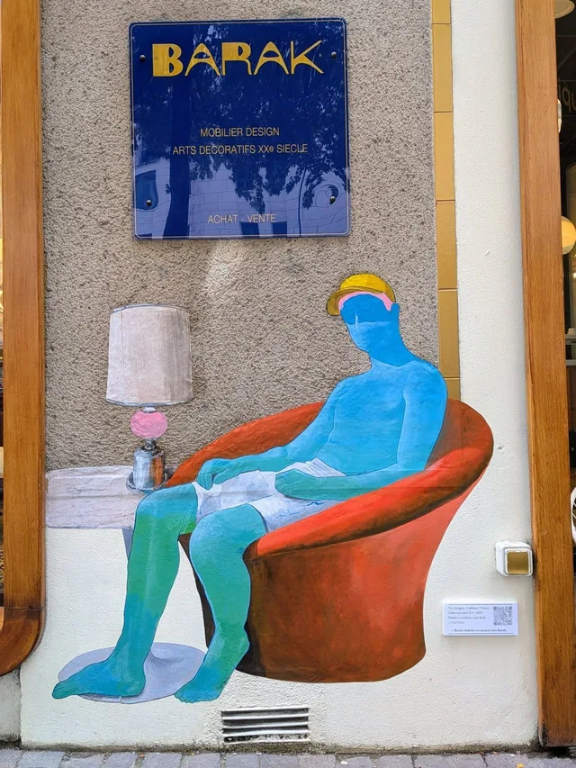 Collage dans une vitrine, personnage bleu assis dans un fauteuil orange près d'une lampe.