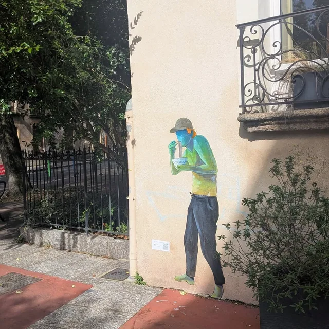 Collage sur une façade claire, personnage debout buvant dans un gobelet devant une grille.