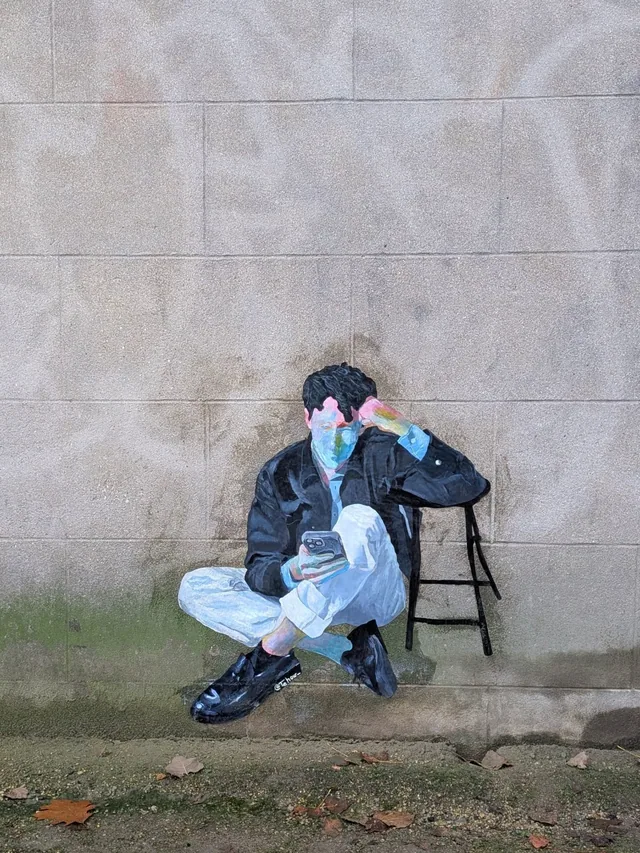Collage sur un mur de pierre, personnage assis sur un tabouret, les mains posées sur le visage.